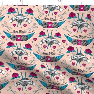 May include: A repeating pattern on a pale peach background features knitting-themed illustrations. The design includes winged yarn balls with skulls, roses, hearts, scissors, and knitting needles. The text "Born to Knit" and "Knitting takes balls" are also present.