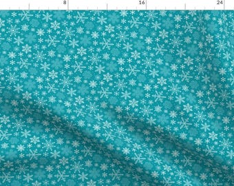 May include: Teal blue fabric with a white snowflake pattern. The snowflakes are of various sizes and are scattered randomly across the fabric.
