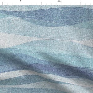 May include: Textile fabric with a watercolor-style design. The pattern features horizontal bands of varying shades of blue and white, creating a wavy, textured appearance. The fabric has a soft, muted color palette.