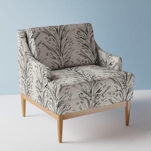 Peut inclure: Un fauteuil doté d'un revêtement en tissu gris clair avec un motif botanique de feuilles et de fleurs gris foncé. Le fauteuil présente un dossier carré, un coussin d'assise épais et quatre pieds en bois clair fuselés.