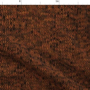 May include: Close-up of a fabric with a repeating pattern of small, interlocking, copper-colored rings. The rings are arranged in a dense, chainmail-like design, creating a textured surface. The overall color is a blend of copper and dark brown.