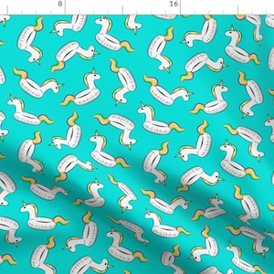 Può includere: Un tessuto blu turchese con un motivo ripetuto di galleggianti per piscina gonfiabili a forma di unicorno bianchi. I galleggianti a forma di unicorno hanno criniere e code arcobaleno.