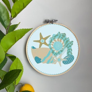 May include: A blue and brown seashell embroidery hoop art piece with a starfish and a blue and white patterned ball. The hoop is made of wood and has a light blue background.