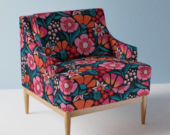 May include: A floral armchair with a black background. The chair features a vibrant pattern of pink, orange, and white flowers with teal leaves. The wooden legs are light brown.