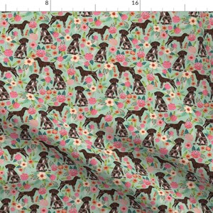 Könnte beinhalten: Ein nahtloses Muster mit braunen und weißen Deutsch Kurzhaar auf hellblauem Hintergrund mit rosa, weißen und grünen floralen Akzenten.