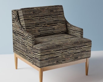 May include: An armchair upholstered in a fabric featuring a horizontal pattern of black, tan, and cream-coloured rectangular blocks. The chair has a square backrest, integrated armrests, and four tapered light-coloured wooden legs.