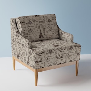 Puede incluir: Un sillón beige con patas de madera presenta un diseño de tela de temática parisina con ilustraciones en blanco y negro de la Torre Eiffel, llaves y el texto "Tramways Paris" y "Vive la France".