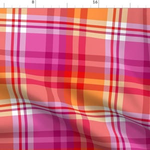May include: A pink, orange, and red plaid fabric with a white stripe. The fabric is folded and has a slight wrinkle.