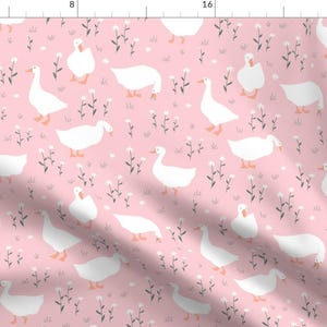 Pode incluir: Um tecido rosa com um padrão repetitivo de gansos brancos e pequenas flores brancas. Os gansos estão virados em direções diferentes e têm um design simples e de desenho animado.