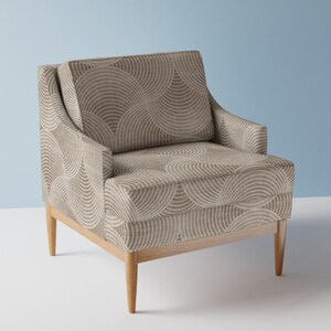 Op de afbeelding: Een bruine fauteuil met een geometrisch patroon van gebogen lijnen. De stoel heeft houten poten en een licht gebogen rugleuning.