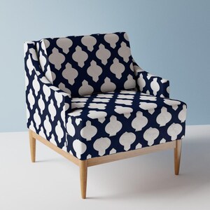 May include: Armchair with a navy blue and white geometric pattern. The chair has a light wood frame and legs. The pattern is a repeating design of white shapes on a navy blue background. The chair has a high back and armrests.