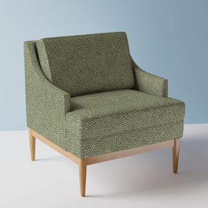 May include: An armchair upholstered in a sage green fabric featuring a repeating pattern of small, light-colored vertical dashes. The chair has a square backrest, integrated armrests, and is supported by four tapered light-colored wooden legs.