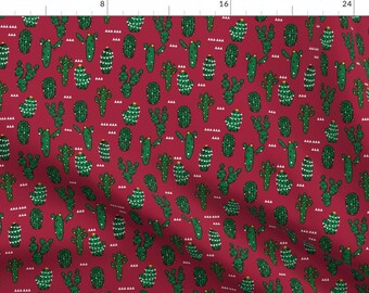 May include: A red fabric with a repeating pattern of green cactus plants decorated with white lights and a gold star on top.