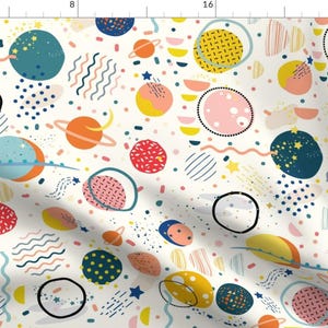 Op de afbeelding: Een grillig stofpatroon met kleurrijke planeten, sterren en abstracte vormen in tinten blauw, oranje, geel, roze en rood op een crèmekleurige achtergrond. Het ontwerp bevat gestippelde en gestreepte elementen, waardoor een speelse, ruimtethema ontstaat.