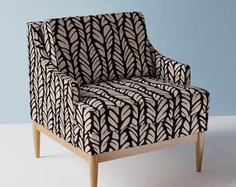 May include: A contemporary armchair featuring a black and cream leaf design. The chair has a light wood frame and legs. The fabric displays a repeating pattern of stylized leaves.