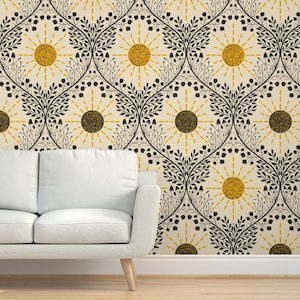 May include: A white sofa sits against a wall adorned with wallpaper. The wallpaper showcases a repeating pattern of stylized suns and floral motifs in black and gold on a cream backdrop. The design evokes a vintage, botanical style.