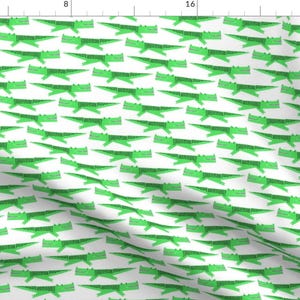 May include: A white fabric with a repeating pattern of green crocodiles. The crocodiles are facing right and have a simple, cartoon-like design.