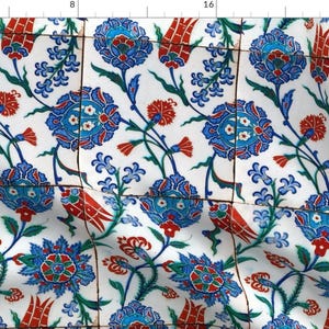 Può includere: Un motivo floreale blu, rosso e verde che si ripete su uno sfondo bianco. Il design ricorda le tradizionali piastrelle turche.