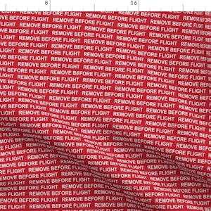 May include: Red fabric with a white repeating pattern of the text "REMOVE BEFORE FLIGHT".