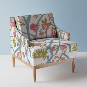 May include: A white armchair with a floral pattern featuring pink flowers and blue branches. The chair has wooden legs and a slightly curved back.