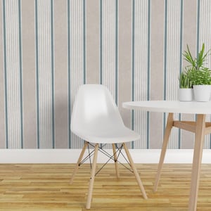 May include: A white molded plastic chair with light wood legs and a black metal wire base, positioned next to a white round table with a green potted plant, set against a wall with vertical stripes in shades of beige, white, and blue.