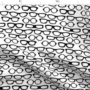 May include: White fabric with a repeating pattern of black eyeglasses in various shapes and styles. The glasses are arranged in a random, all-over design, creating a visually interesting texture.