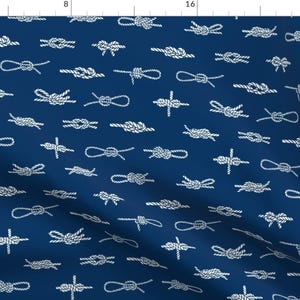 Può includere: Un tessuto blu navy con un motivo bianco ripetuto di nodi marini. I nodi sono di varie forme e dimensioni.
