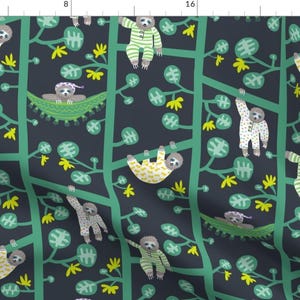 May include: A dark blue fabric with a repeating pattern of green branches, yellow flowers, and sloths in various poses. Some sloths are sleeping in hammocks, others are hanging from branches, and some are wearing pajamas.