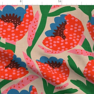 Op de afbeelding: Bloemenstof met een herhaald patroon van grote, gestileerde bloemen. De bloemen zijn voornamelijk rood met witte stippen, blauwe centra en groene stelen en bladeren. Roze accenten en een crèmekleurige achtergrond maken het ontwerp compleet.