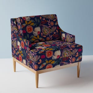 Könnte beinhalten: Ein marineblauer Sessel mit einem lebendigen Blumenmuster in Orange, Rosa, Gelb und Weiß. Der Stuhl hat hellfarbene Holzbeine und Armlehnen und bietet einen modernen Touch. Das florale Design bedeckt den gesamten Stuhl.