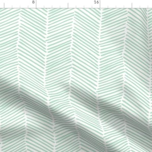 May include: A white fabric with a repeating pattern of light blue, hand-drawn chevron shapes.