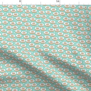 May include: A teal blue fabric with a repeating pattern of white and brown donuts with white frosting and brown sprinkles. The donuts have a smiling face with two black eyes and a brown mouth.