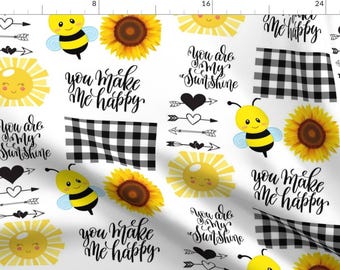 May include: A white background with a repeating pattern of yellow suns, black and white checkered squares, black and white arrows, black hearts, and bumblebees. The text "You make me happy" and "You are my sunshine" is repeated throughout the pattern.