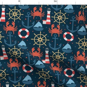 Op de afbeelding: Een donkerblauwe stof met een herhalend patroon van rode krabben, vuurtorens, ankers, scheepswielen en reddingsboeien. Het patroon is in nautische stijl.
