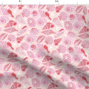 Op de afbeelding: Een roze stof met een herhalend patroon van rode en roze schelpen. De stof is perfect voor knutselprojecten, quilten en decoratie in huis.