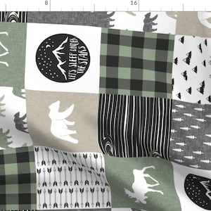 Peut inclure: Un tissu patchwork avec différents motifs de créatures de la forêt, y compris des orignaux, des ours et des flèches. Le tissu est dans des tons de vert, noir et blanc, avec un motif répétitif de carreaux, de rayures et de formes géométriques. Le texte "Let's Sleep Under The Stars" est présenté dans un cercle noir.