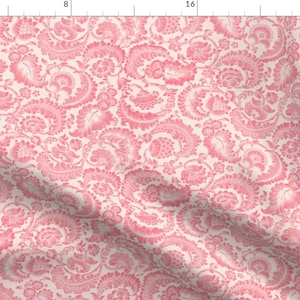 May include: A pink and white paisley patterned fabric with a subtle sheen. The fabric has a repeating pattern of stylized floral and paisley motifs.