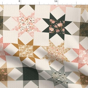 Könnte beinhalten: Ein Patchwork-Quilt mit einem Sternmuster. Der Quilt verwendet Stoffe in Creme, Rosa, Gold und Dunkelgrün. Einige Sterne haben florale Muster, während andere Karomuster oder unifarbene Designs aufweisen. Der Quilt kombiniert geometrische und florale Elemente.