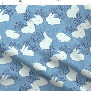 Puede incluir: Un patrón sin costuras con conejos blancos sobre un fondo azul. Los conejos están dibujados en un estilo simple y caprichoso y están rodeados de pequeños diseños florales.