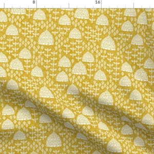 May include: A seamless pattern featuring a repeating design of white beehives on a mustard yellow background. The beehives are stylised and have a textured appearance. The background has a subtle diamond pattern.
