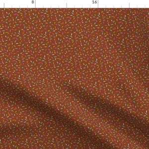 Peut inclure: Un tissu brun avec un motif répétitif de vermicelles colorés. Les vermicelles sont dans différentes nuances de rose, orange, jaune et bleu.