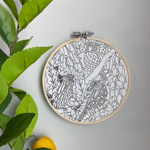 May include: A black and white embroidery hoop with a design of three birds in a forest setting. The birds are detailed with intricate patterns and surrounded by leaves and acorns.