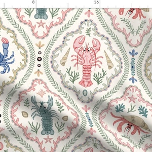 May include: A fabric pattern featuring a repeating design of blue crabs, pink lobsters, and sea creatures enclosed in ornate, light pink and beige decorative frames. The background is off-white with small green seaweed and star accents.