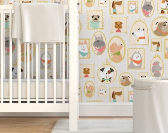 Op de afbeelding: Een wit wiegje met een wit wiegdek en een witte wasmand voor een muur met een patroon van honden in gouden frames. De honden zijn allemaal van verschillende rassen en hebben verschillende uitdrukkingen.