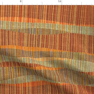 May include: A woven fabric with a striped pattern in shades of orange, red, yellow, brown, and blue. The fabric has a textured surface and a slightly irregular weave.