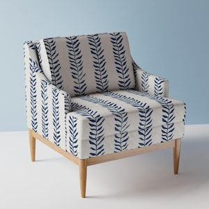 Può includere: Una poltrona con rivestimento in tessuto beige chiaro caratterizzata da un motivo verticale ripetuto di foglie blu scuro simili a felci. La sedia presenta uno schienale quadrato, un cuscino di seduta spesso e quattro gambe in legno chiaro.