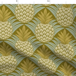 Op de afbeelding: Een herhalend patroon van gestileerde ananassen in crème en goud, tegen een olijfgroene en lichtblauwe achtergrond. Het ontwerp doet denken aan vintage behang.