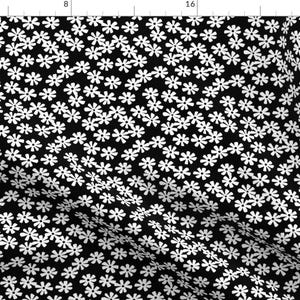 以下が含まれることがあります： 白い花柄の黒い布。花は小さく、シンプルで幾何学的なデザインです。