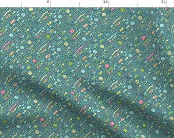 Op de afbeelding: Een tealblauwe stof met een herhalend patroon van kleurrijke abstracte vormen. De vormen zijn in tinten groen, geel, roze en blauw.