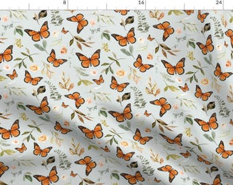 Könnte beinhalten: Ein nahtloses Muster mit orangefarbenen Schmetterlingen auf hellblauem Hintergrund. Die Schmetterlinge sind von grünen Blättern und kleinen weißen Blüten umgeben.